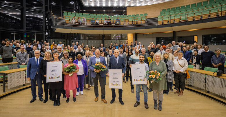 Große Gruppe im Plenarsaal mit Empore, mehrere Personen halten Urkunden und Blumen für den Sächsischen Integrationspreis
